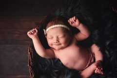 Glückliches Baby in Körbchen mit dunklem Fell