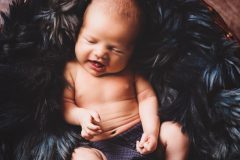 Baby schlafend in Körbchen auf dunklem Fell