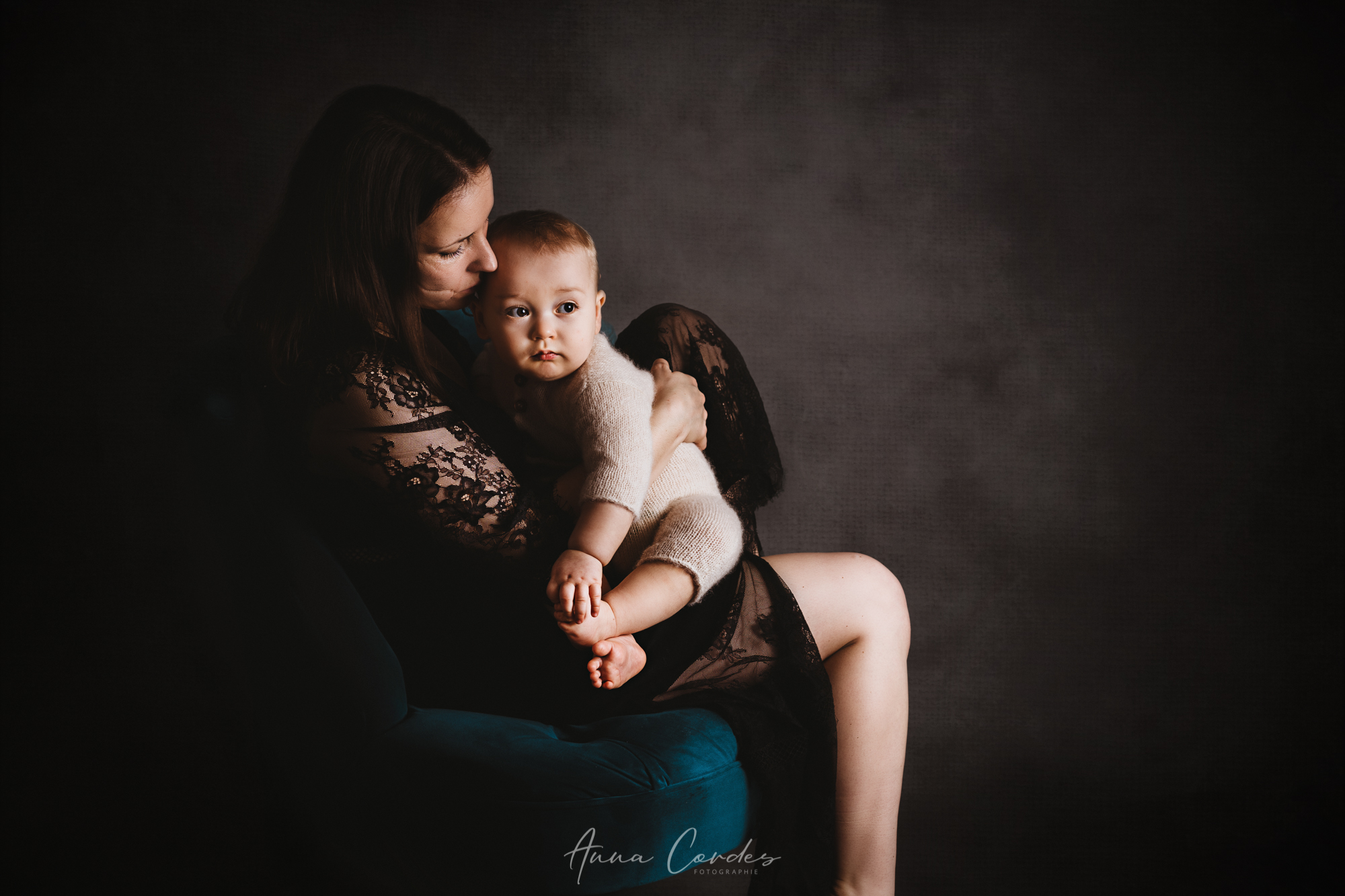 Mutter h&auml;lt ihr Baby im Arm vor einem dunklen, k&uuml;nstlerischen Hintergrund.
