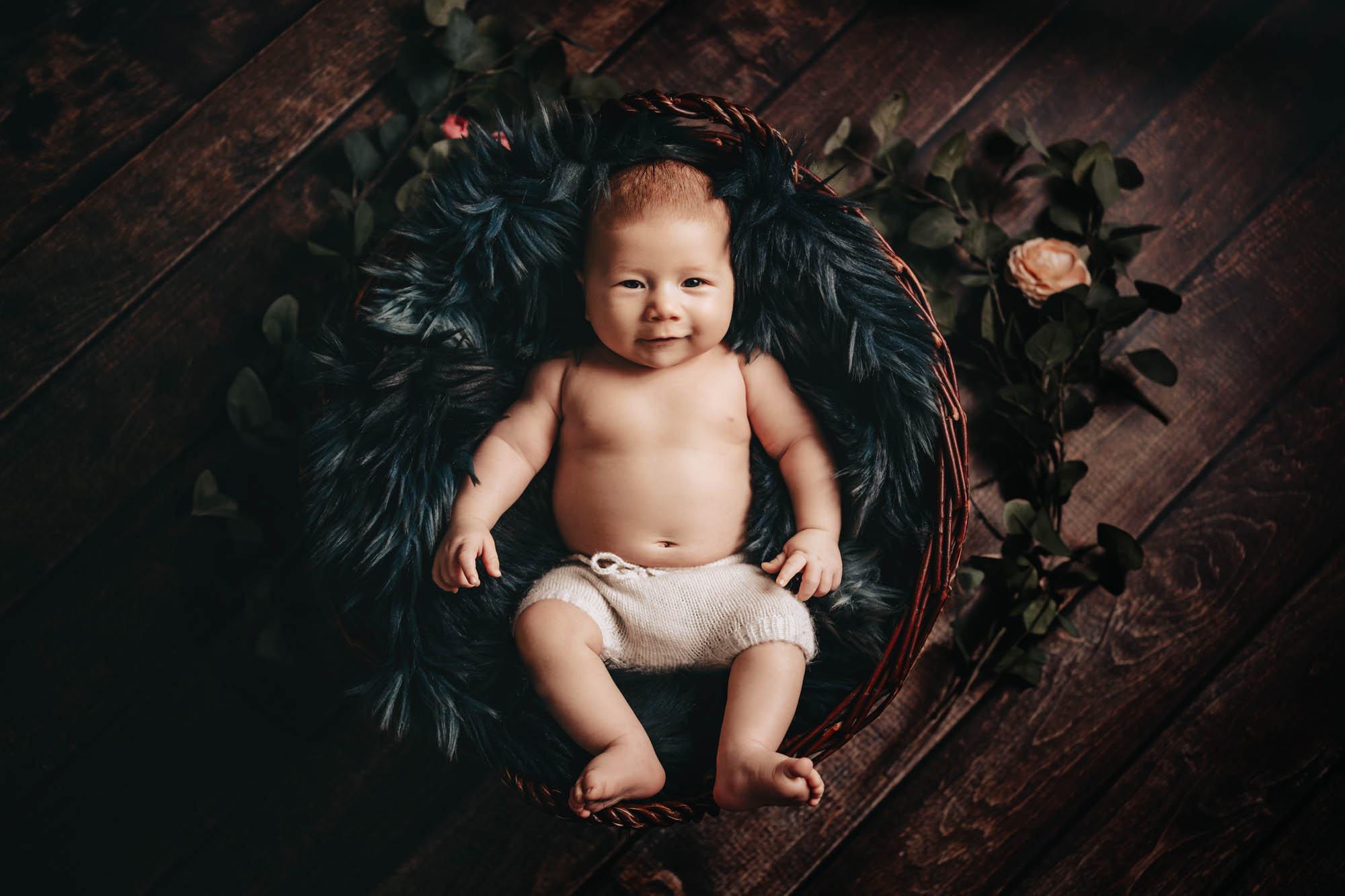 Meilenstein Shooting Wien: Baby sitzt neugierig in einem rustikalen Korb bei einem herbstlichen Setup