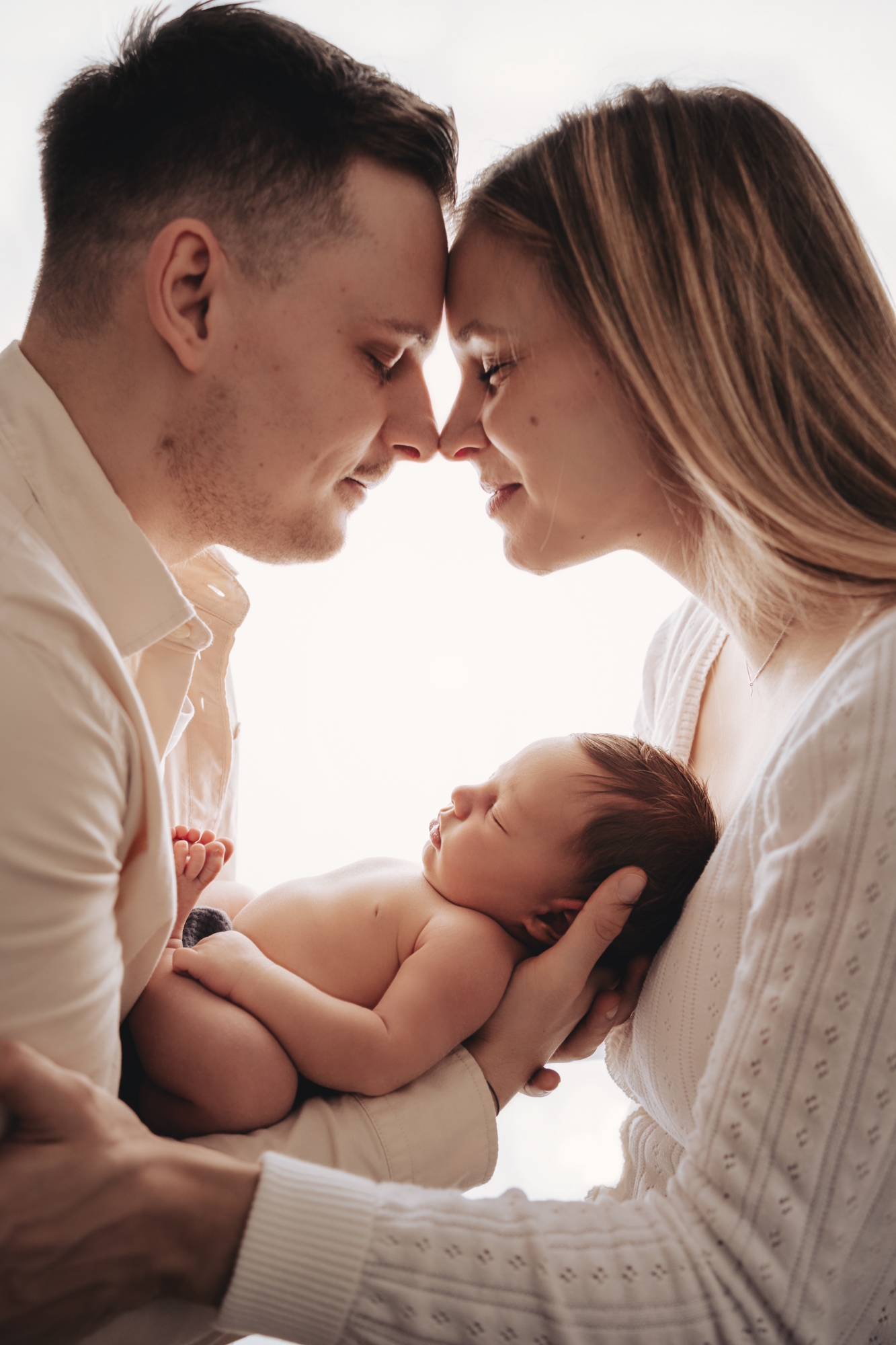 Mama und Papa halten das Neugeborene zwischen sich, ganz innig liegen ihre K&ouml;pfe aneinander.