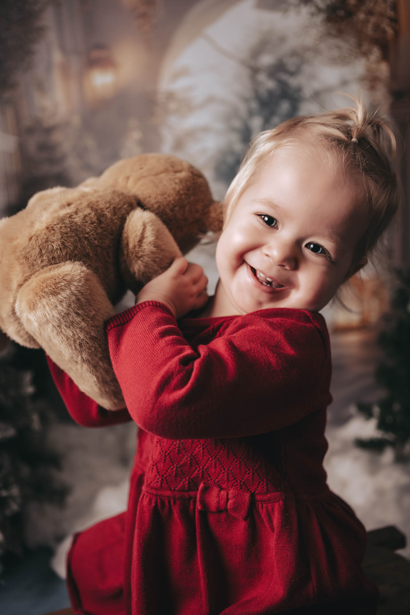 M&auml;dchen im roten Kleid h&auml;lt lachend einen gro&szlig;en Teddyb&auml;ren im Arm.