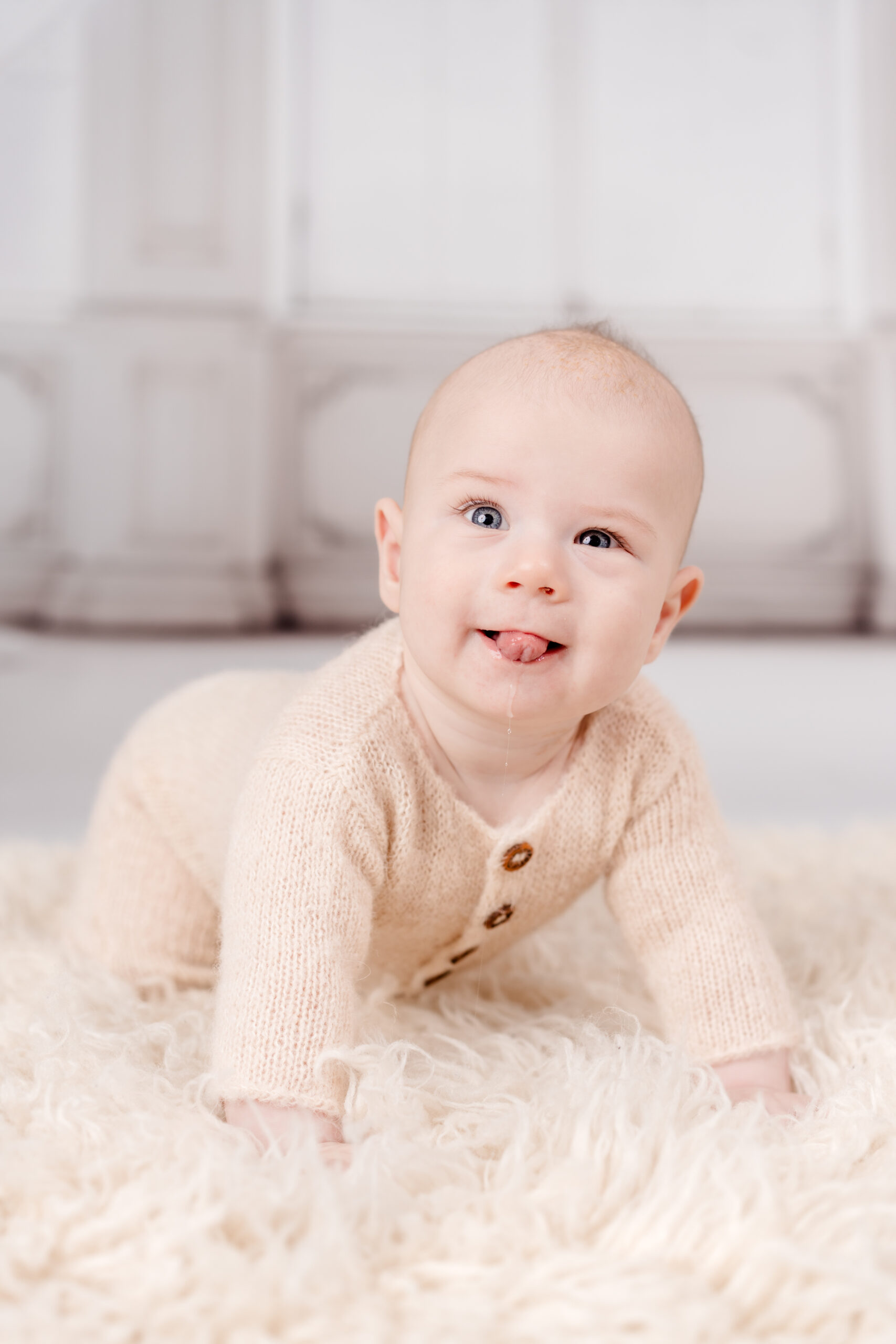 Babyfotograf Wien: Ein lächelndes Baby im hellen Strickoutfit krabbelt neugierig auf einem weichen Teppich