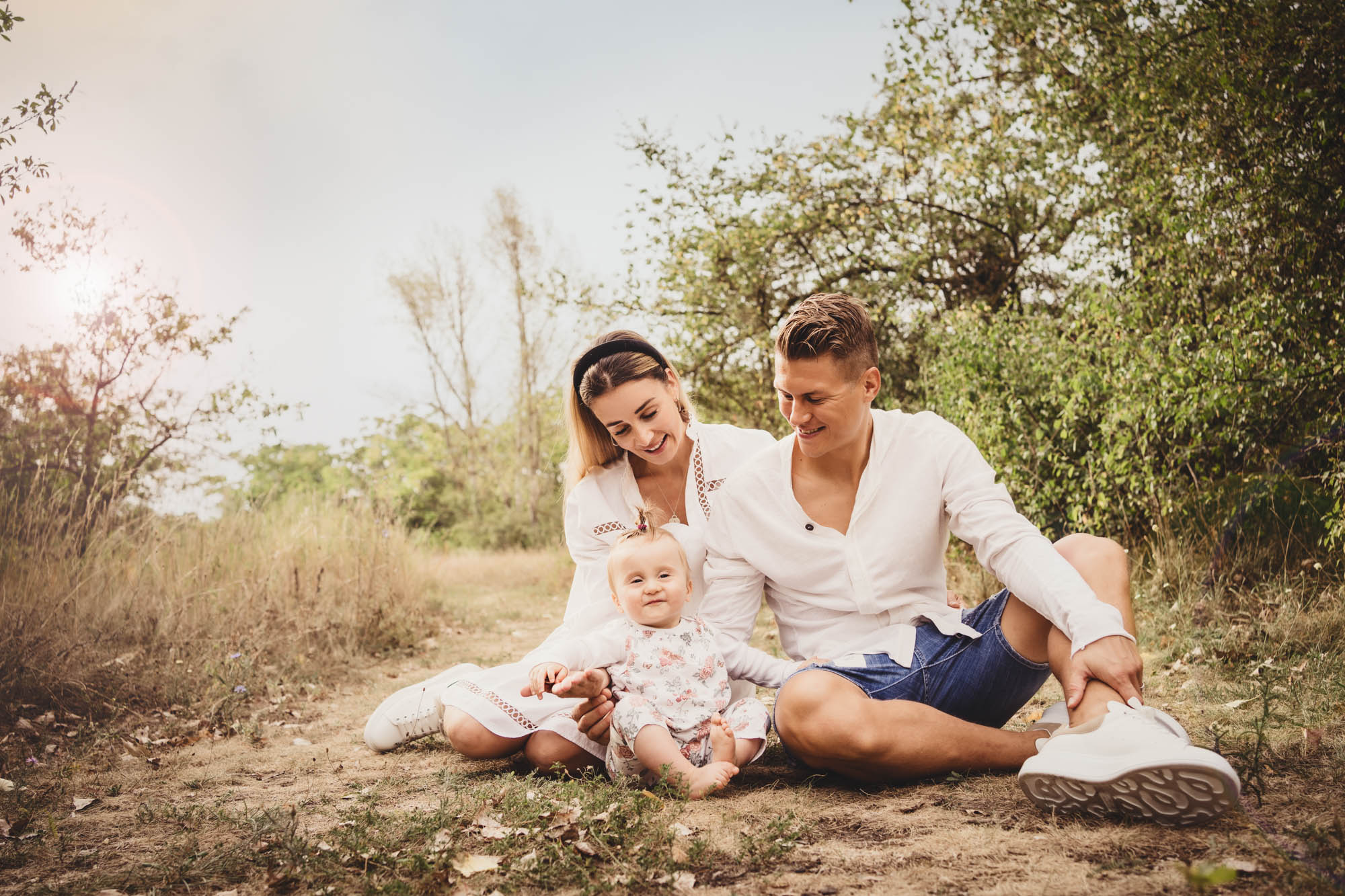 Familie in hellen Outfits posiert in einem sommerlichen Feld.