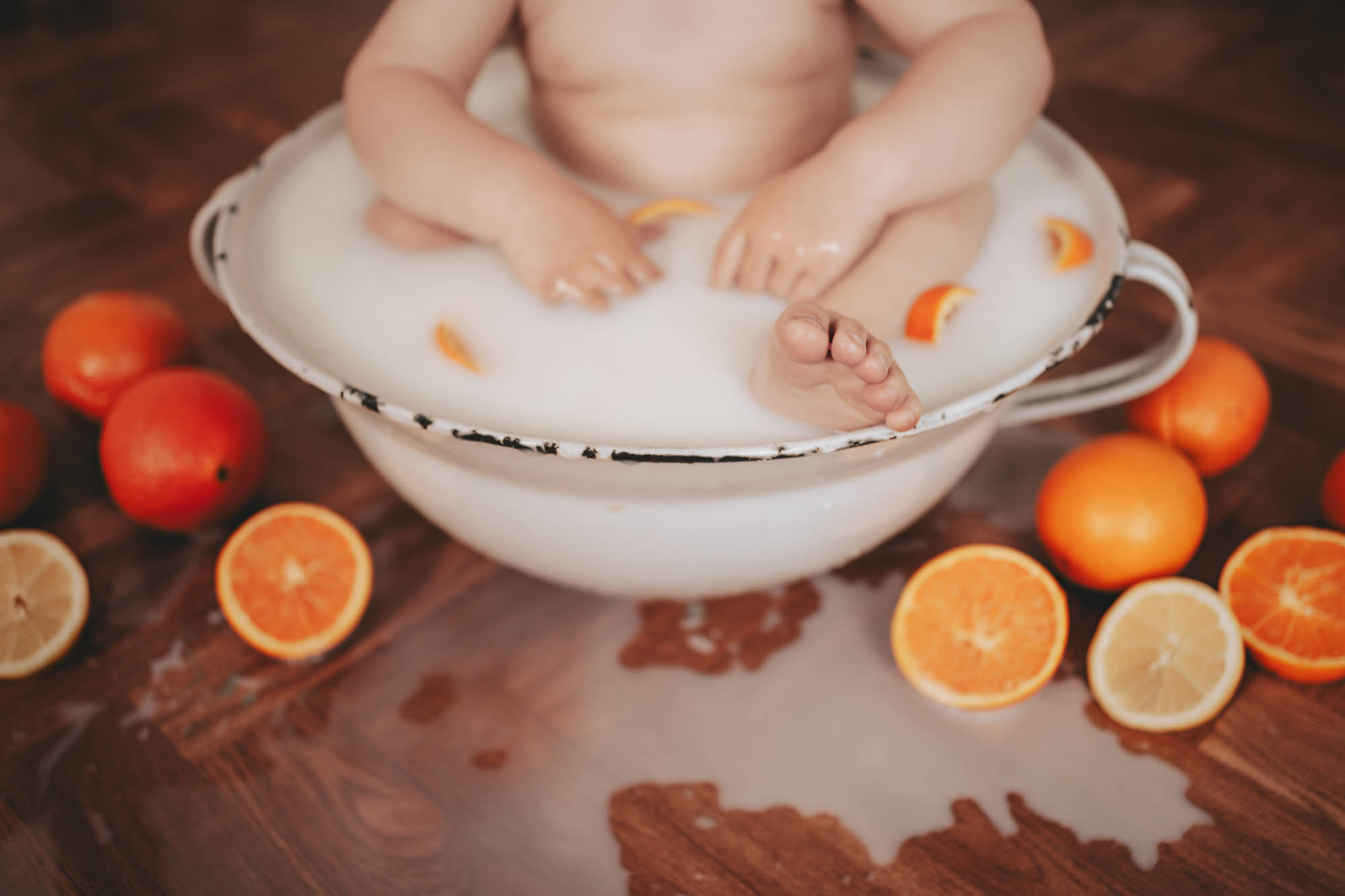 Detailaufnahme von Babyf&uuml;&szlig;en in einem Milchbad mit schwimmenden Orangenscheiben.