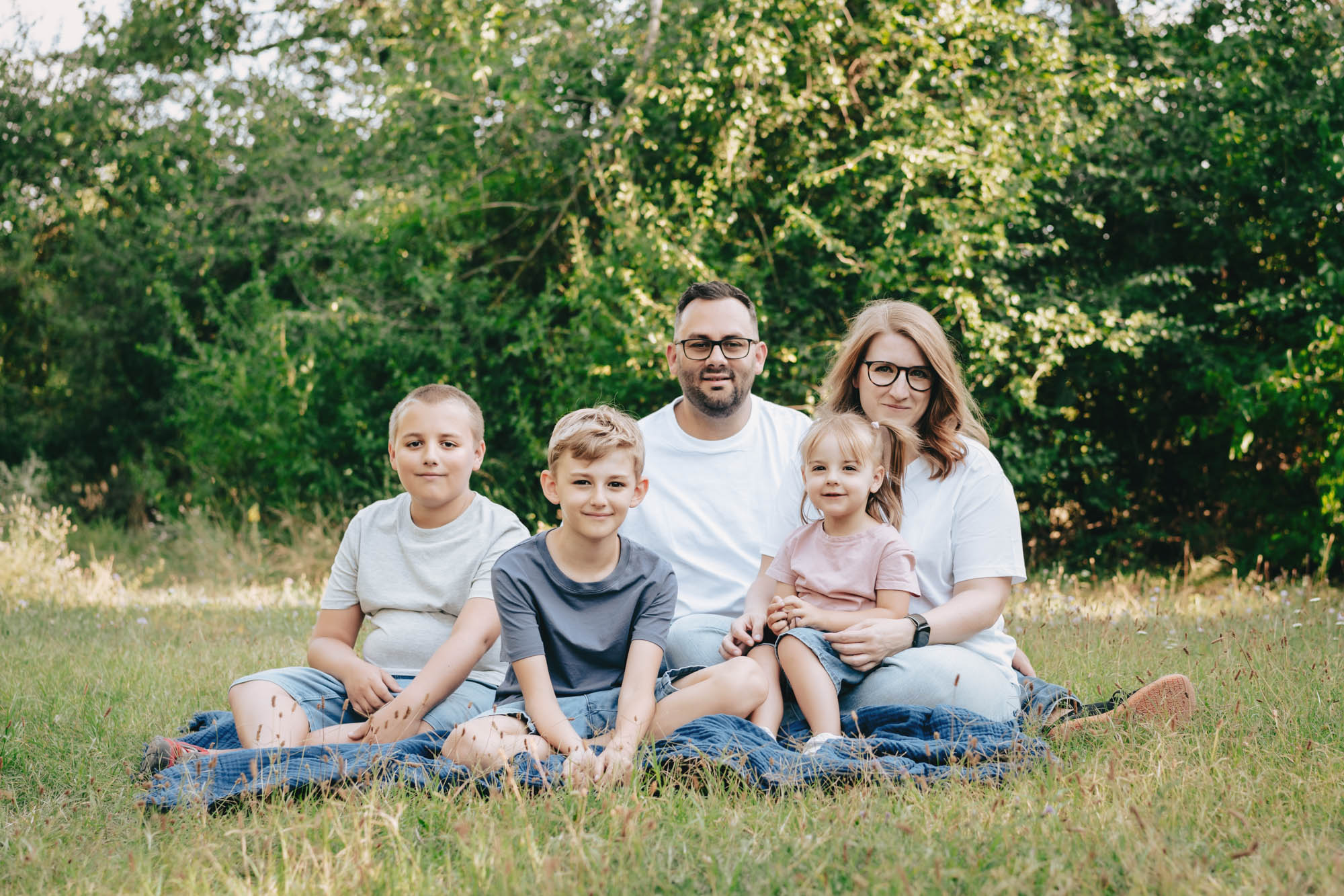 Eltern und drei Kinder sitzen l&auml;chelnd auf einer Wiese.