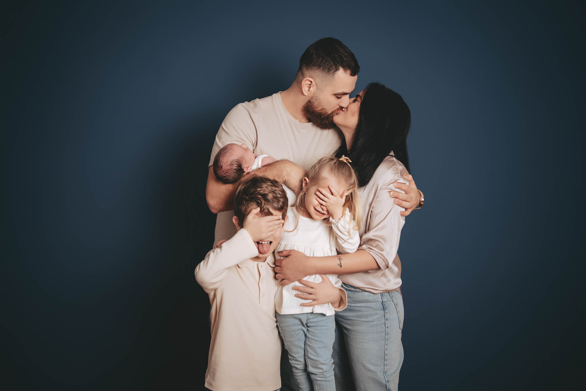 Studioaufnahme einer vierk&ouml;pfigen Familie mit Neugeborenem vor blauem Hintergrund.