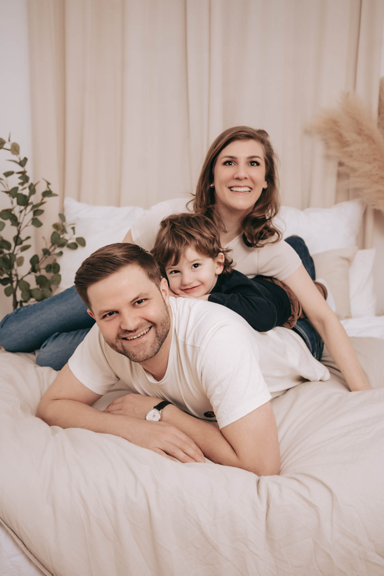 Eltern und Kind kuscheln gemeinsam in einem gro&szlig;en, hellen Bett.