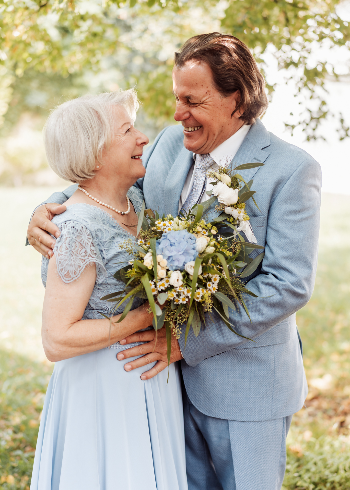 Ein l&auml;chelndes &auml;lteres Brautpaar umarmt sich herzlich bei einer Hochzeit im Freien.