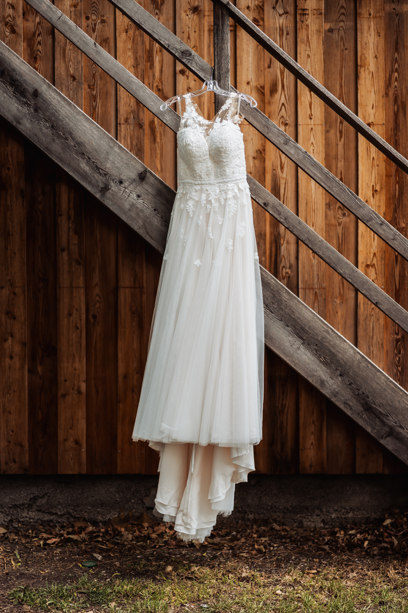 Wei&szlig;es Hochzeitskleid h&auml;ngt an einer rustikalen Holztreppe.