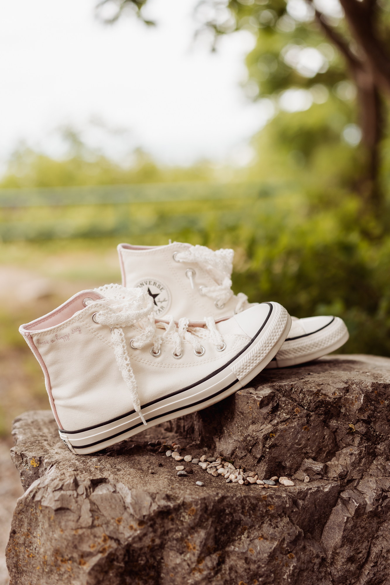 Wei&szlig;e Braut-Sneaker mit Spitzenapplikationen stehen auf einem Stein im Freien.